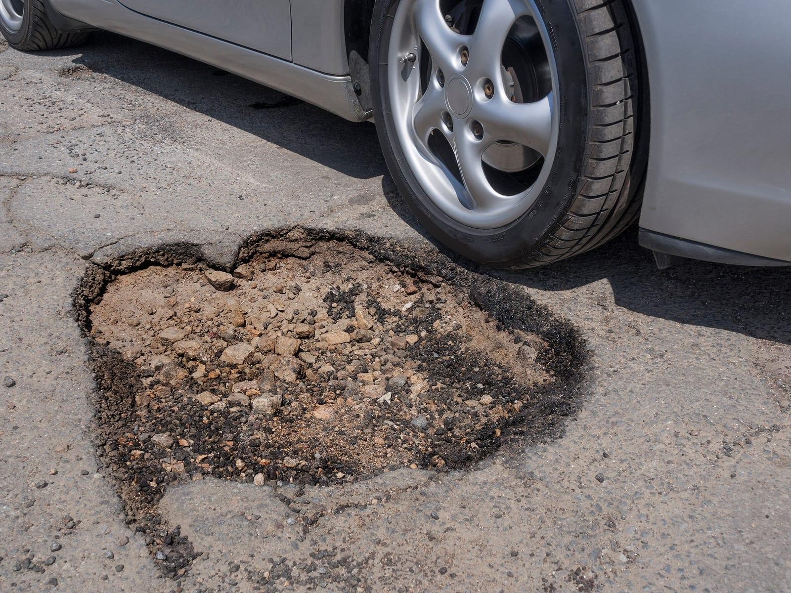 Car tire narrowly missing a large pothole