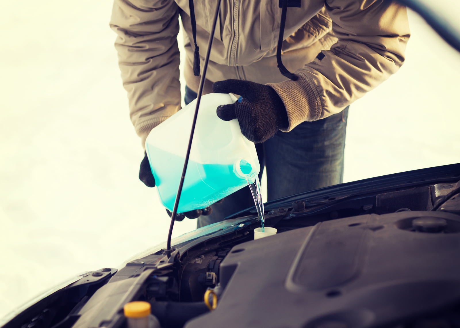 A man pouring windshield washer fluid into his car