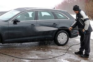 A man washes the dirt and salt off his car in winter
