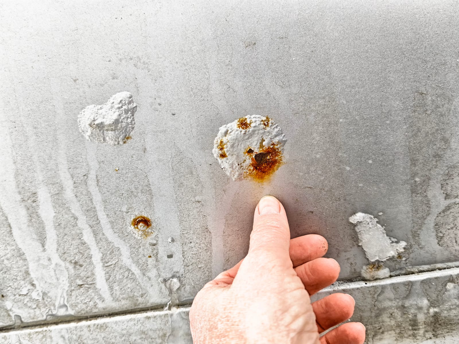 Close-up view of rust and corrosion on car body with hand pointing to damage during vehicle inspection