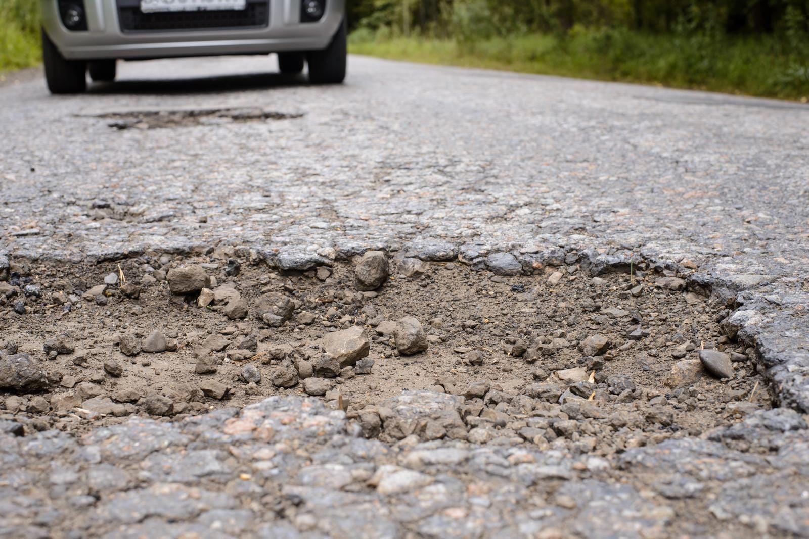 Pothole in asphalt road and car in the background