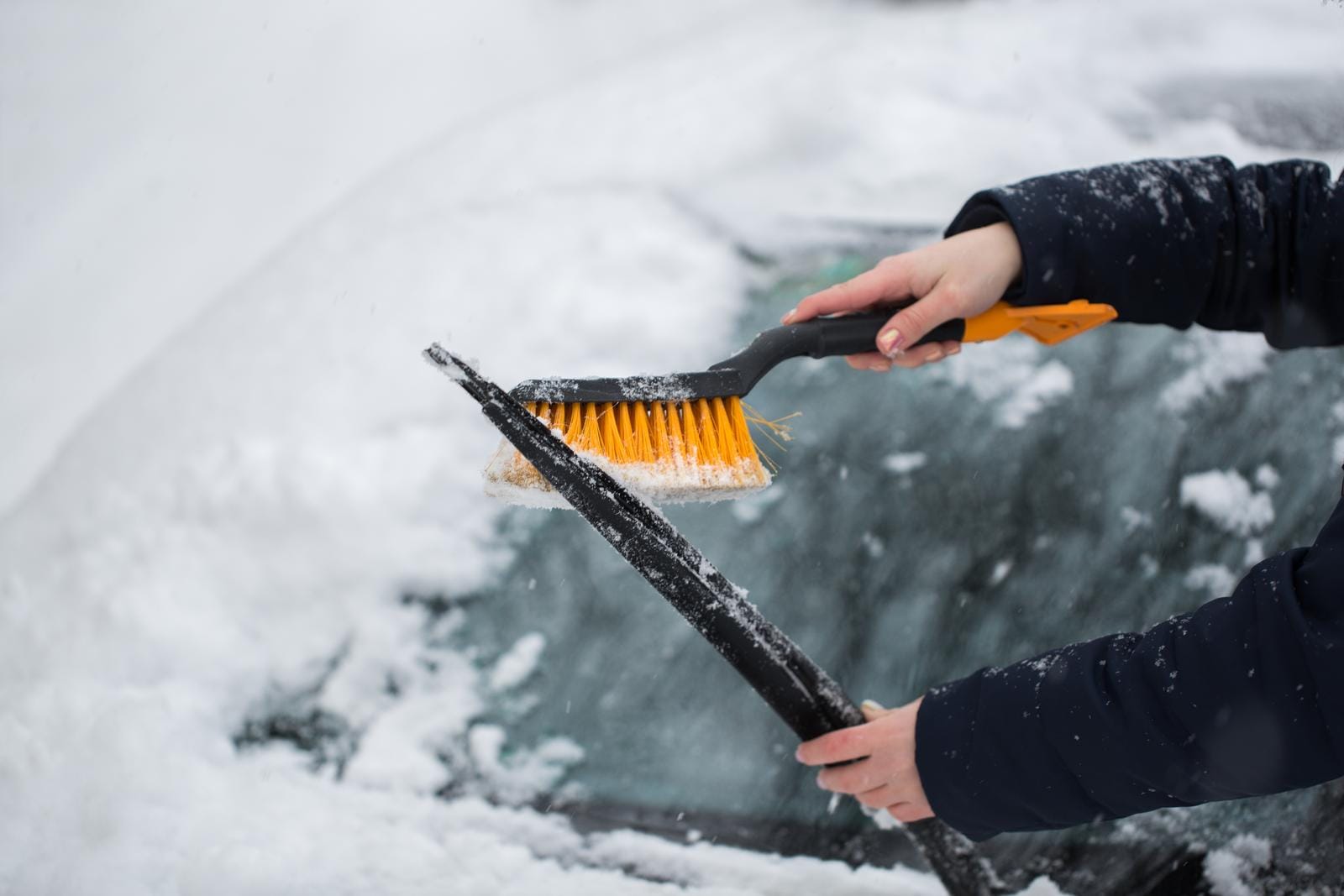 Woman cleaning snow from the car in the winter.