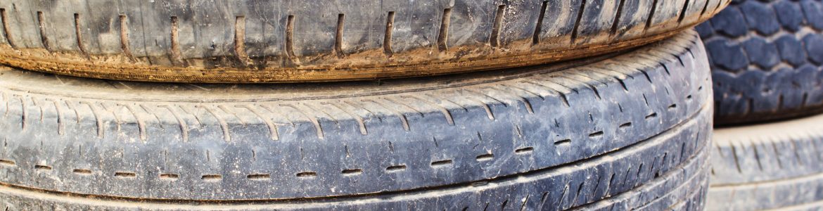 A photo of a stack of dirty old tires with diverse types and depth of tread